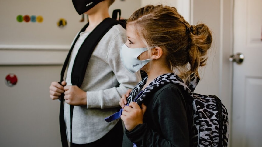 a young girl and boy in masks and wearing backpacks