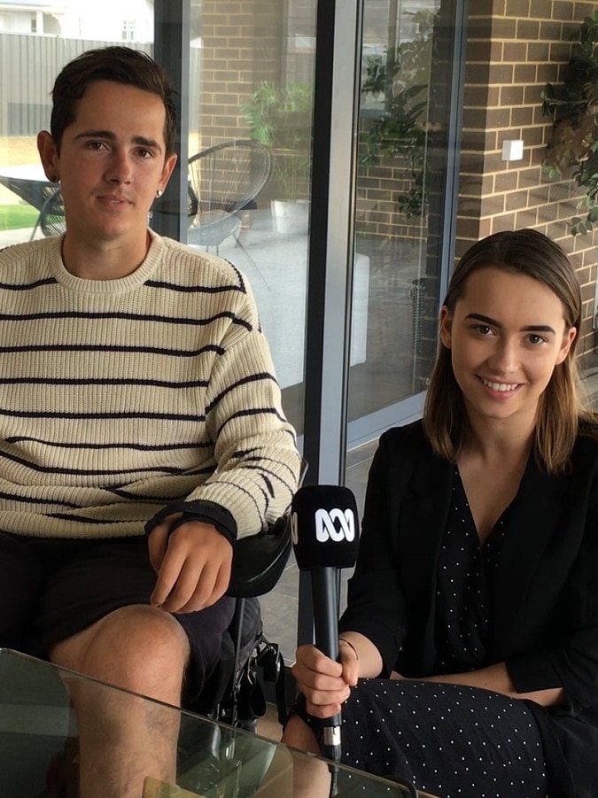 A man in a wheelchair and a woman kneeling, holding an ABC microphone.