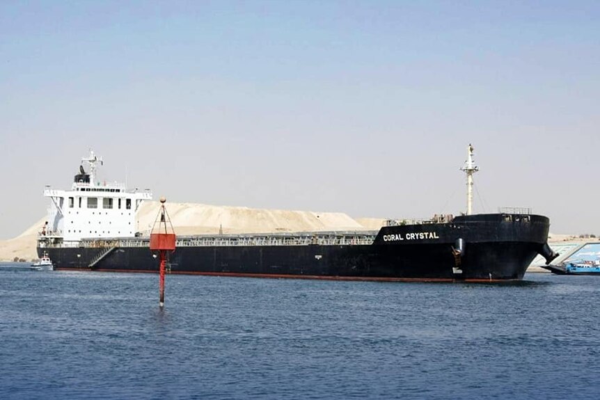 A black bulk carrier ship with the words "coral crystal" written on the hull. 