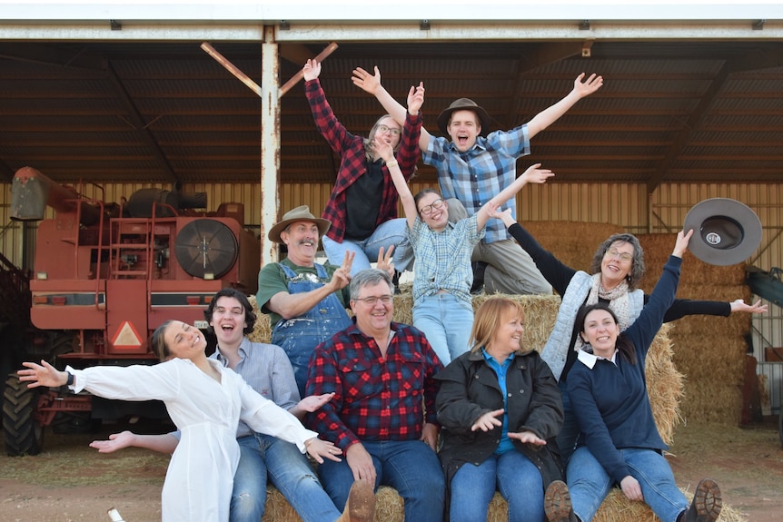 People sitting on a hay bale with their hands in the air in front of an agricultural shed