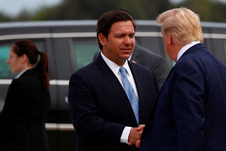 Ron DeSantis smiles and shakes hands with Donald Trump
