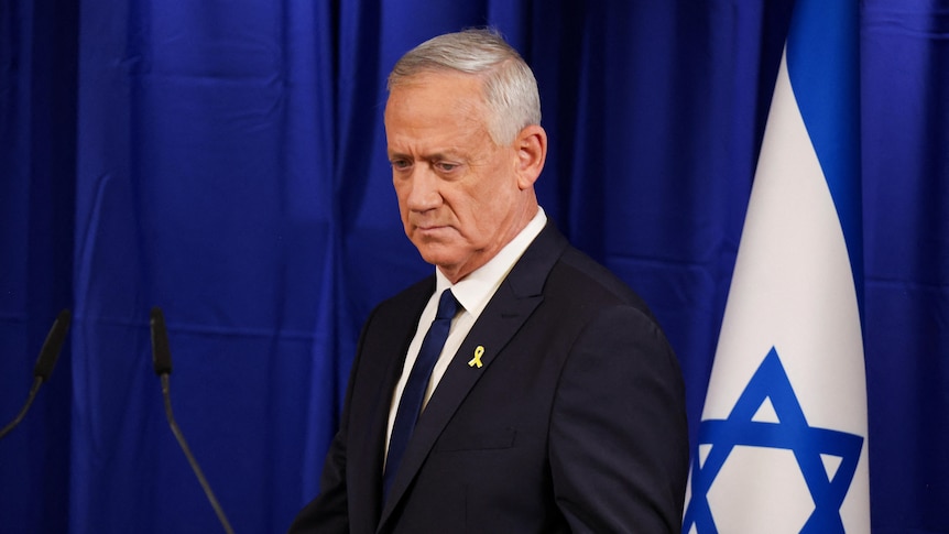 A man walks up to a microphone in front of an Israeli flag.