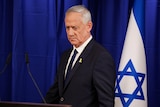 A man walks up to a microphone in front of an Israeli flag.