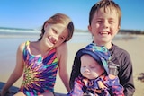 Baby Austin and his siblings at the beach wearing bathers.