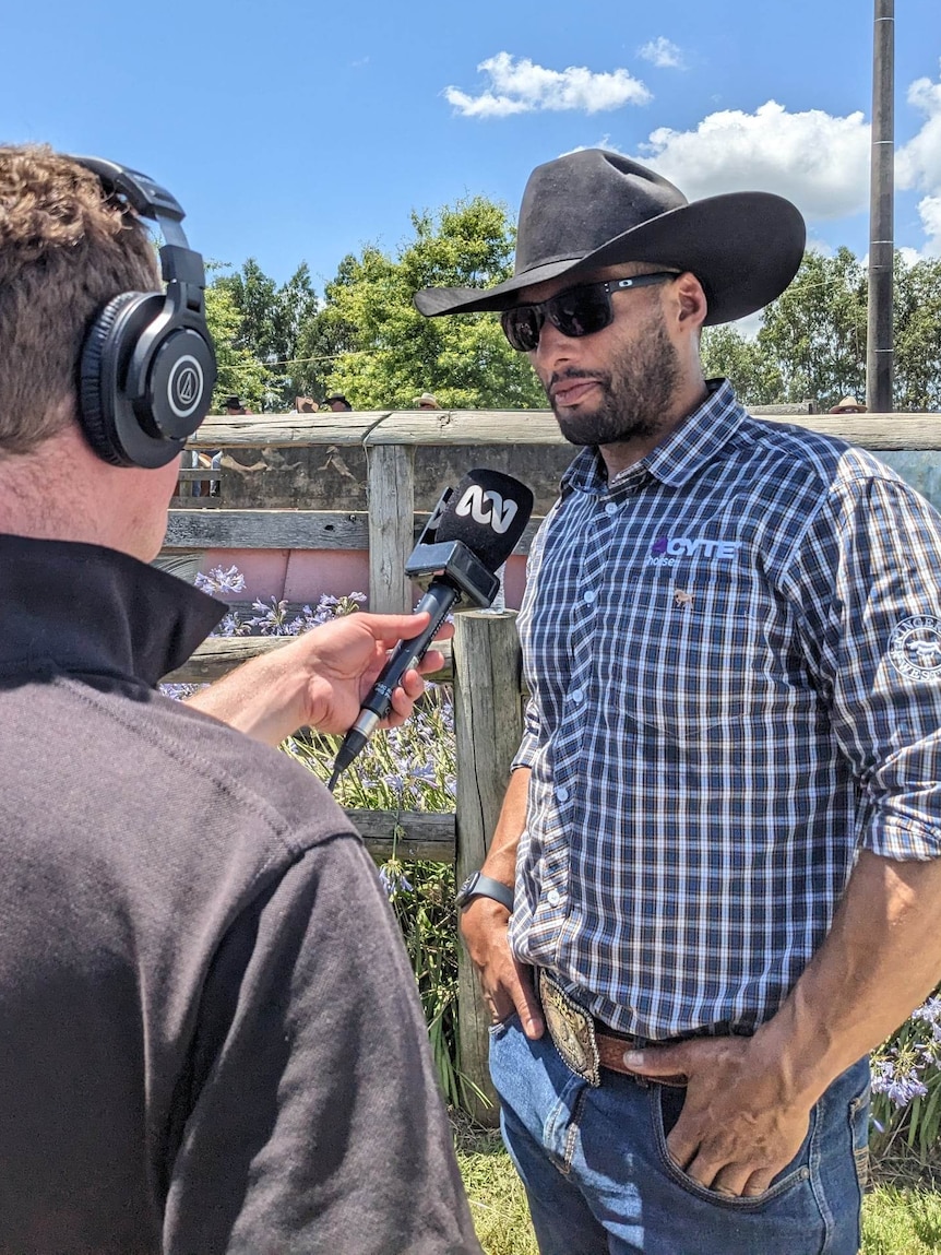 Josh Gibson wearing a broadbrimmed hat and sunglasses is interviewed by an ABC journalist. 