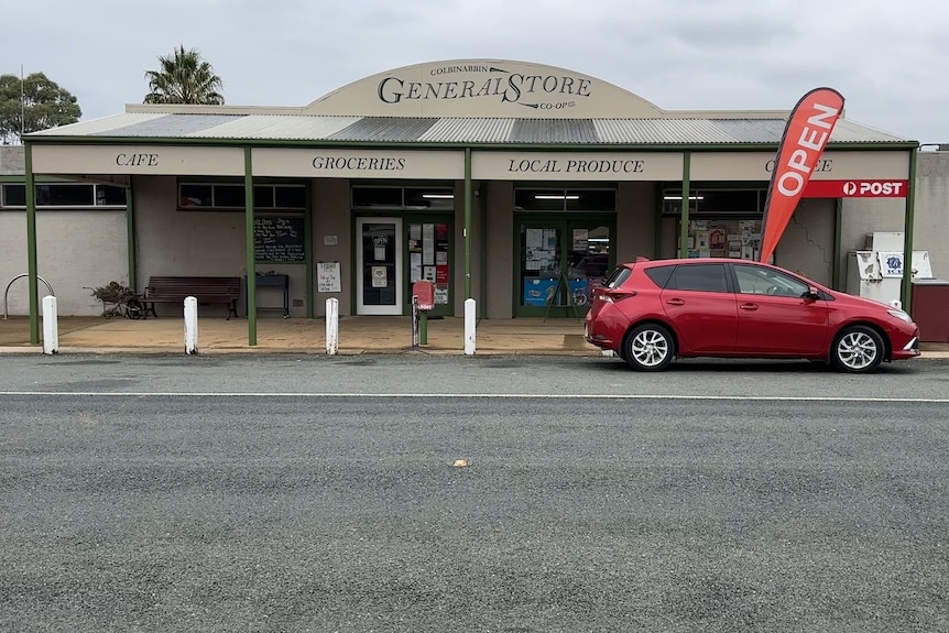 A red car is parked outside a shop in a rural town.