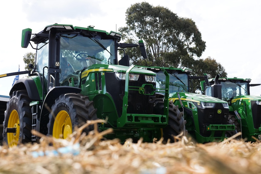 Three green tractors fresh from the assembly line sit on the grass