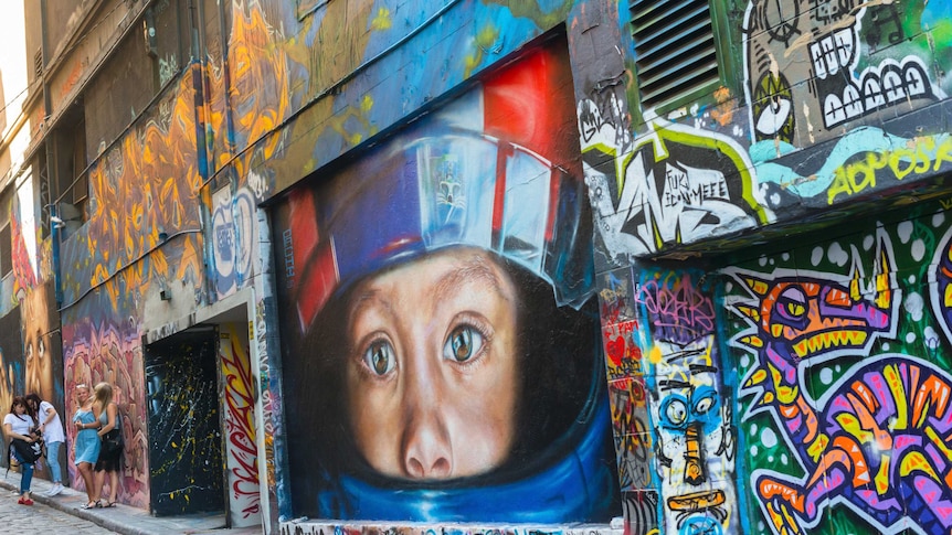 A large wall painted brightly with different words and images, and the large head of a child wearing a helmet at the centre