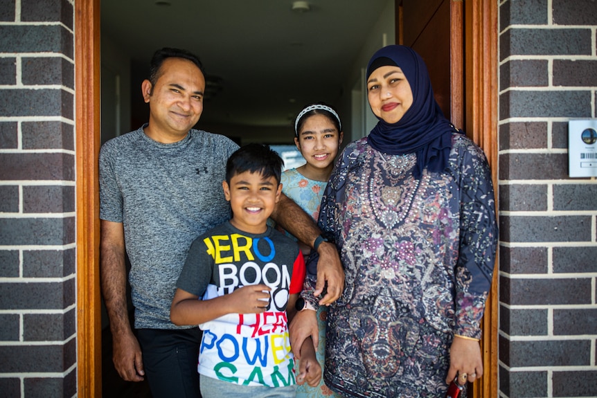 family of four smiles in doorway to house