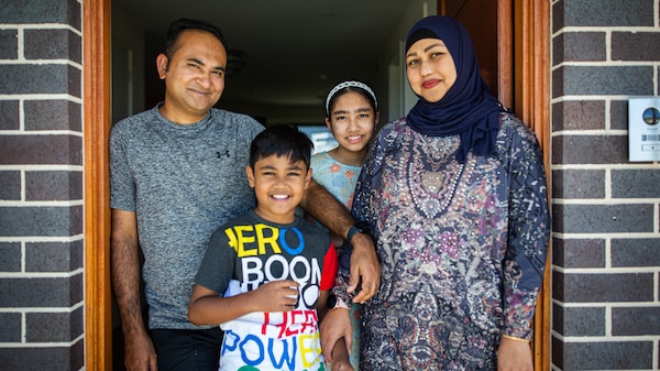 family of four smiles in doorway to house