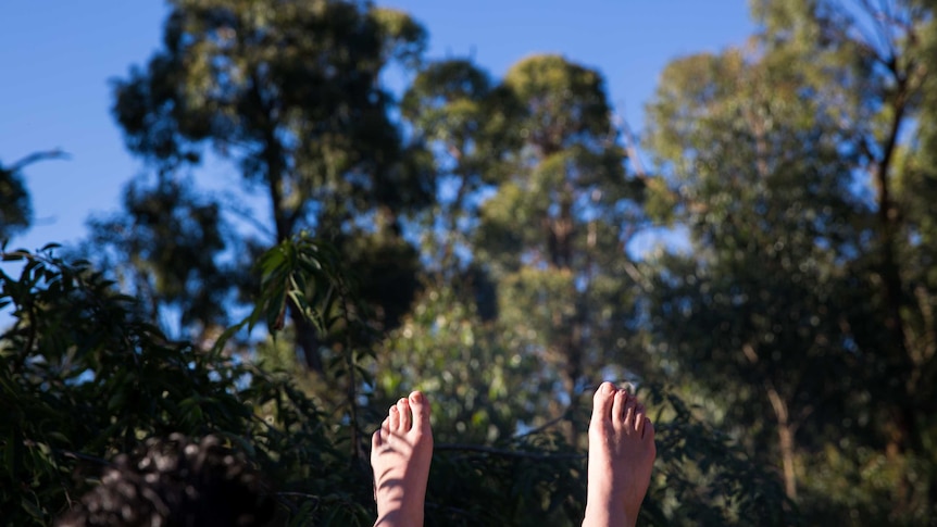 Bare feet catch the sun against a backdrop of green bush and blue sky.