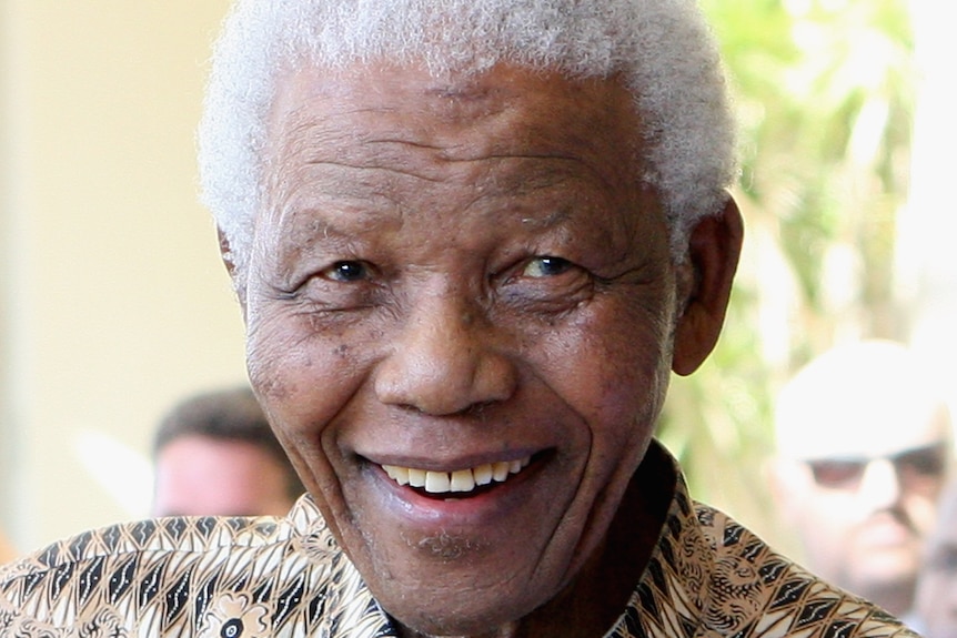 A close-up image of a man smiling widely, with grey have and a print shirt.