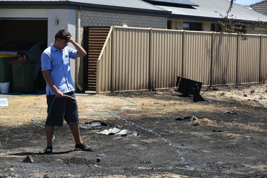 A boy in school uniform hoses burned ground. 