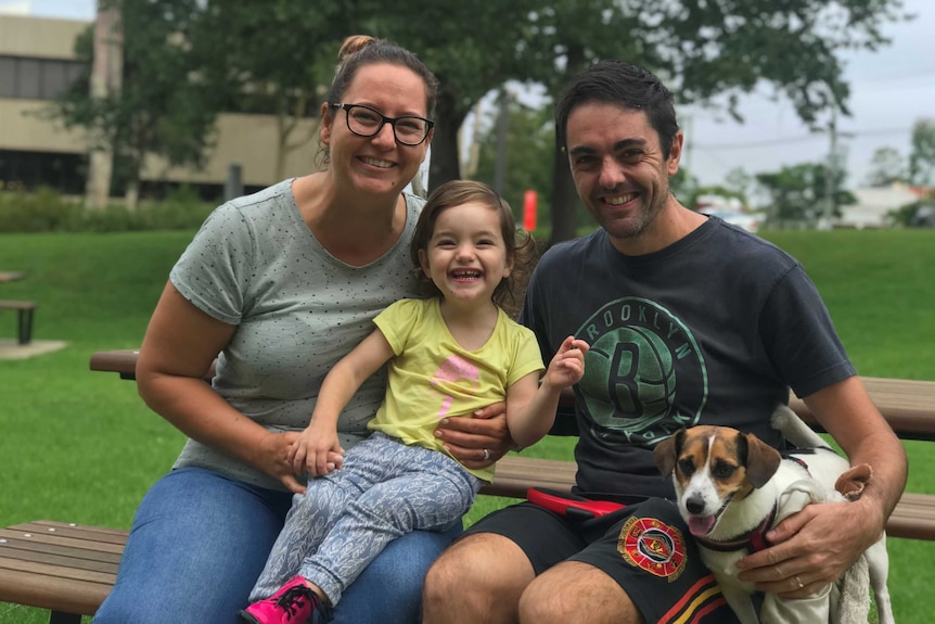 A man and a woman wwith their daughter sit on a park bench.