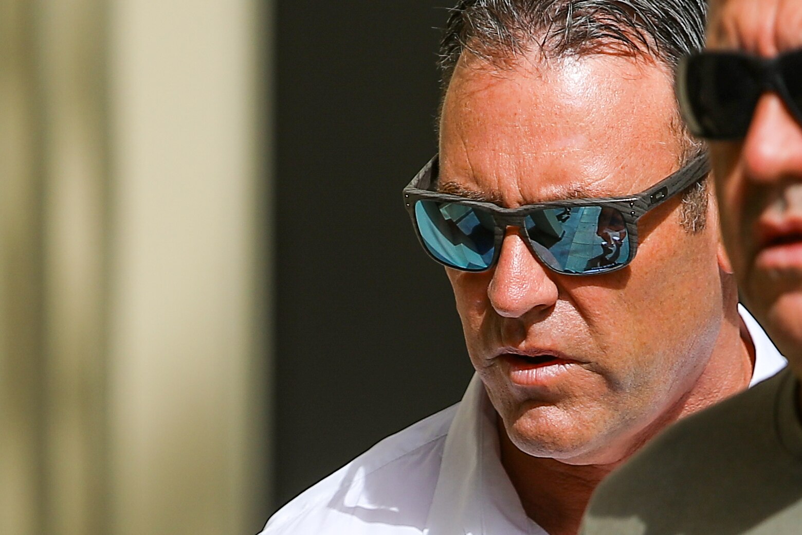 A close-up shot of a middle-aged man with dark hair and mirrored sunglasses.