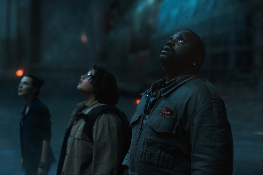 Millie Bobby Brown, Julian Dennison and Brian Tyree Henry looking up concerned in the film in Godzilla vs. Kong