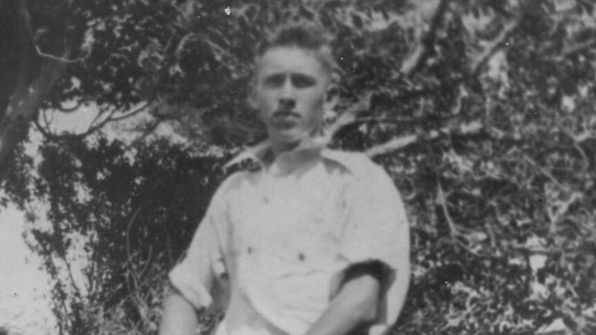 A black and white photo of a young man standing next to a push bike in a garden.