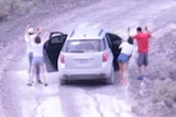 A video screenshot shows four adults standing outside a car with their hands in the air while armed personnel watch