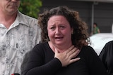 A woman, with dark curly hair, crying while supported by other people around her.