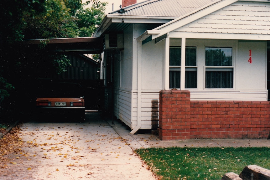 A shot of an old, quite basic house with a brick fence and a car parked in the driveway