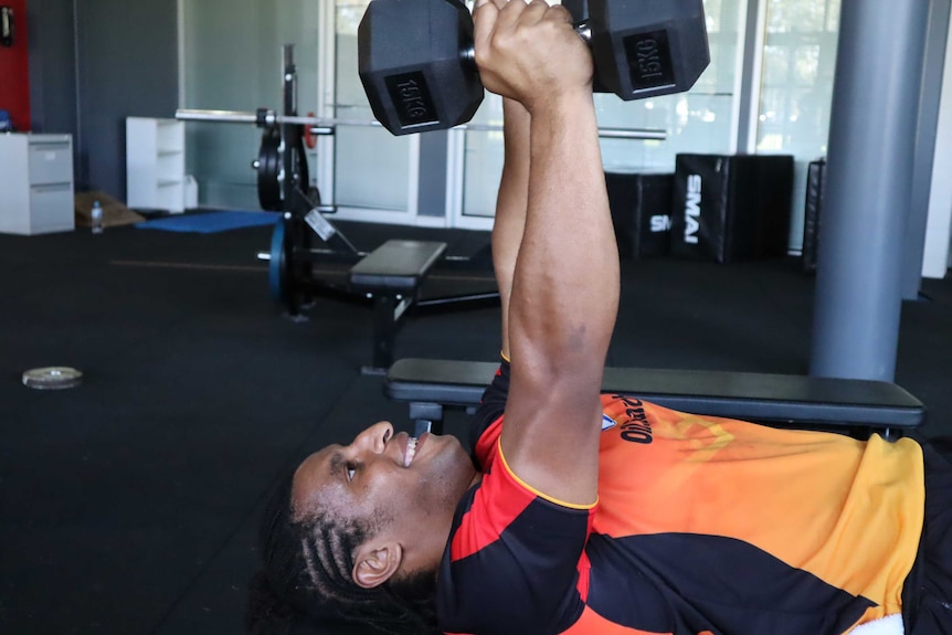 Elsie Albert lifts two dumbbells above her head while laying horizontal on a bench in a gym.