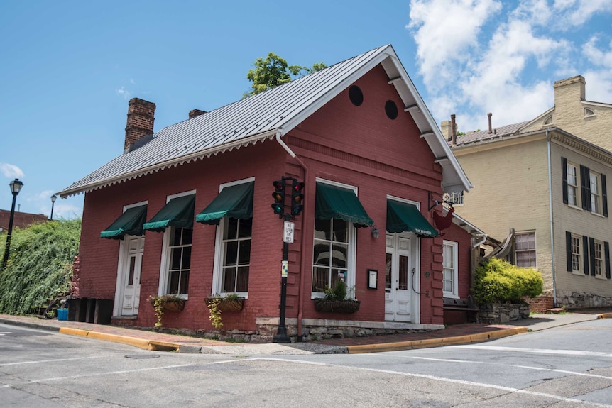 A tiny red brick building on the corner of a rural street in virginia.