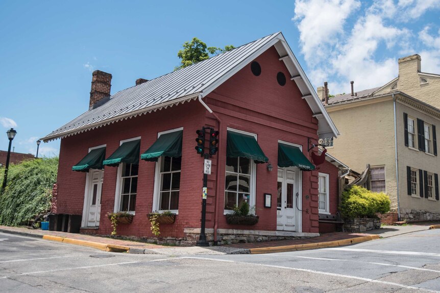 A tiny red brick building on the corner of a rural street in virginia.