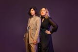 Carrie Brownstein and Corin Tucker stand side-by-side against a purple background