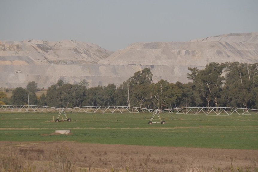 A coal mine in the background with green farmland in foreground.