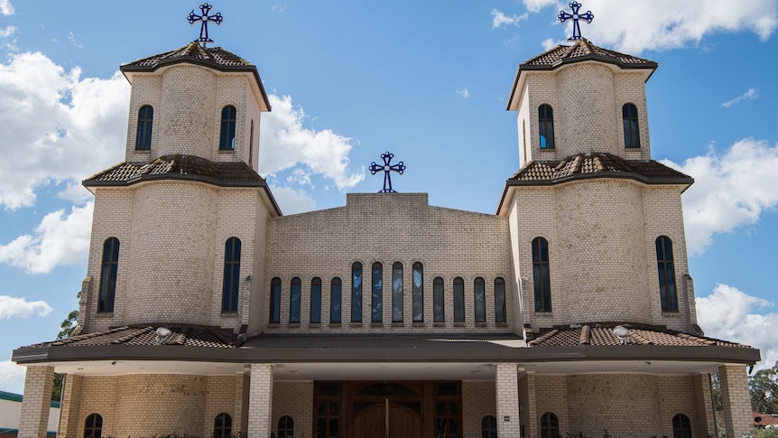 A tall, brick church with two towers is adorned with several crosses.