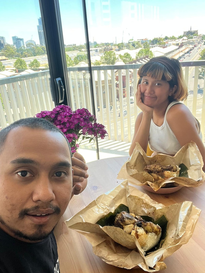 A selfie of a woman and a man sitting on the terrace facing a table with their meals on it.