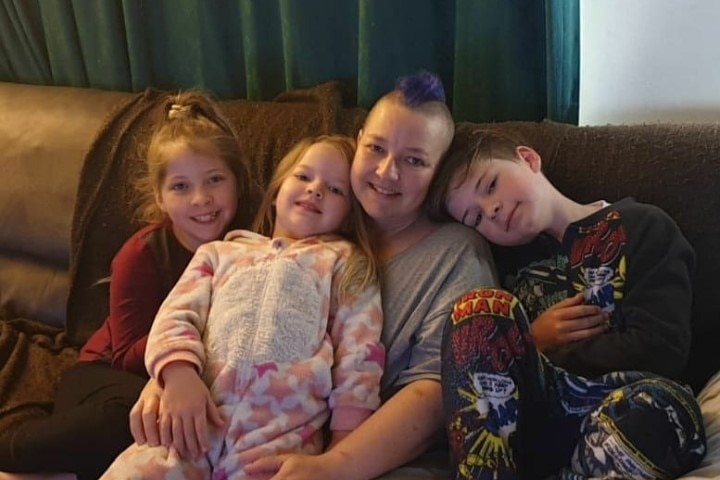 MJ sits on a couch with her three kids, she has purple hair.