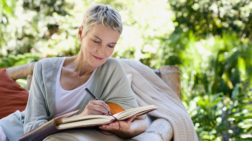 Grey-haired woman writing in a journal in her garden