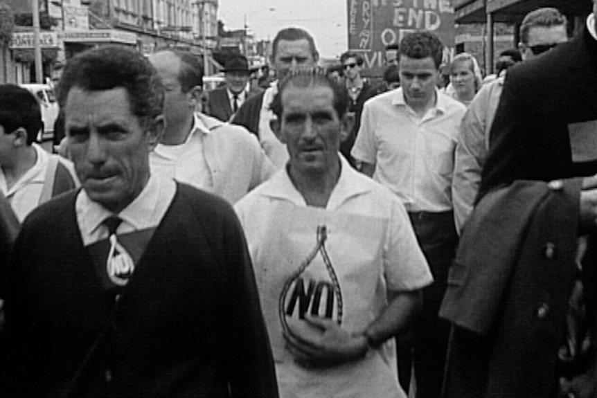 A historical black-and-white image of protesters marching against capital punishment down a busy street