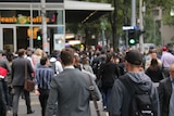 Crowds of pedestrians walk across a city street.