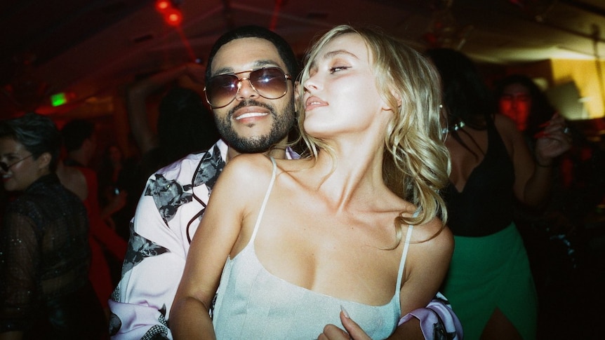 Abel Tesfaye and Lily Rose Depp in The Idol, with Tesfaye holding Depp from behind.