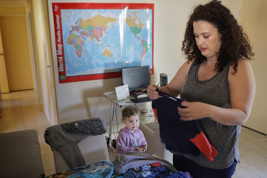 A woman folds clothes while a child watches.