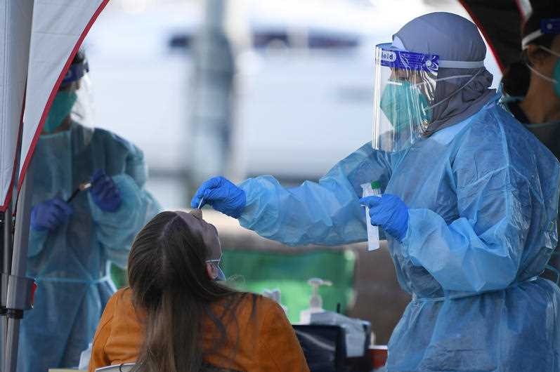 A person getting swabbed for COVID-19 by a nurse in blue hazmat sui.