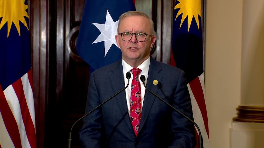 Man speaks at a podium with Malaysian flags behind him.