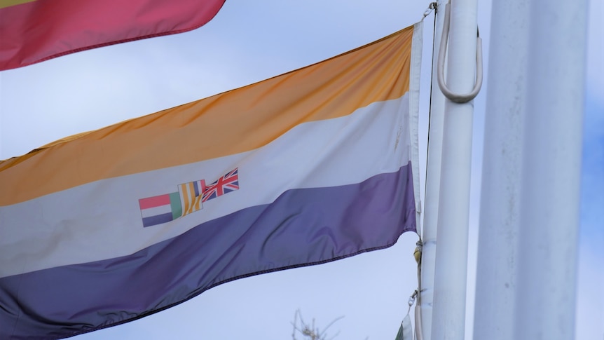 A tri-coloured flag with bars of white flying on a pole.