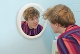 A man in a blue room looking into a mirror.