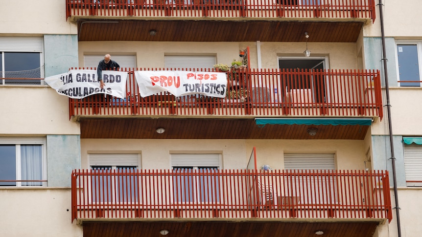 A man places two white banners with red and black writing on balcony fencing.