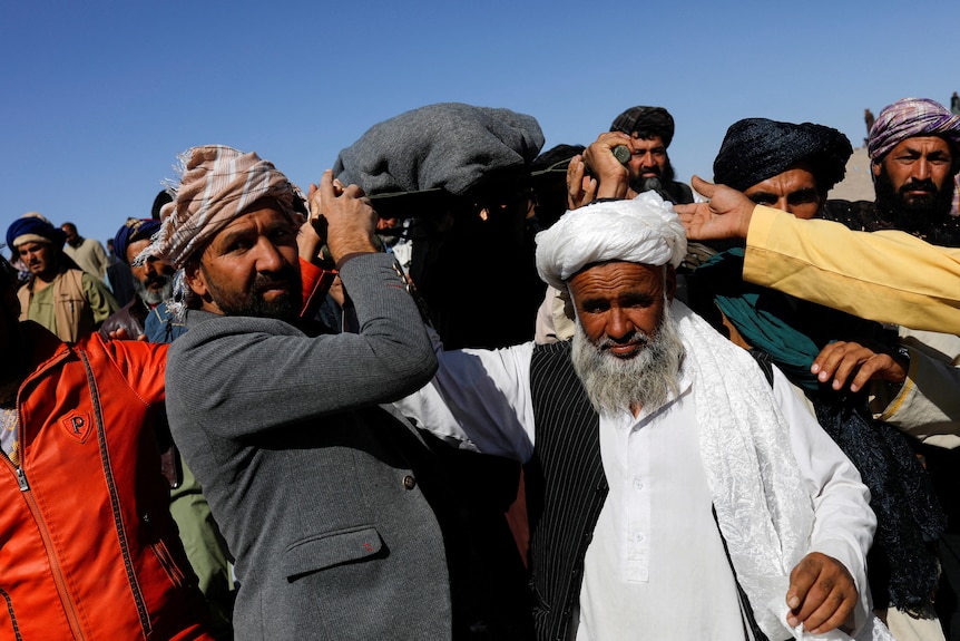 Afghan men carry on their shoulders the body of a woman earthquake victim, wrapped in black cloth.