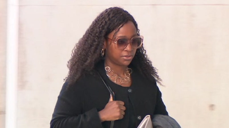 Esther clutches her bag and coat and walks outside court wearing sunglasses.