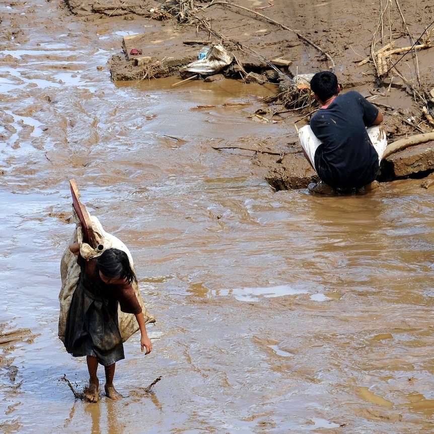 A girl carries salvaged belongings down a muddied street in the wake of Typhoon Washi.