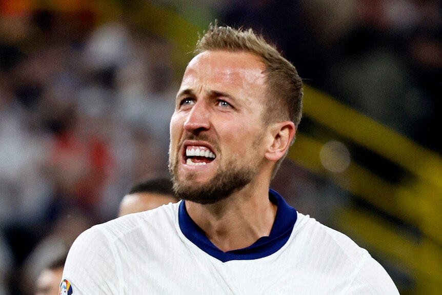  Harry Kane pulls at his England jersey and looks up at a stadium crowd