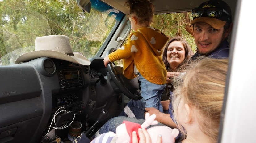 A man laughs inside his ute with two young girls with his wife leaning in through the window.