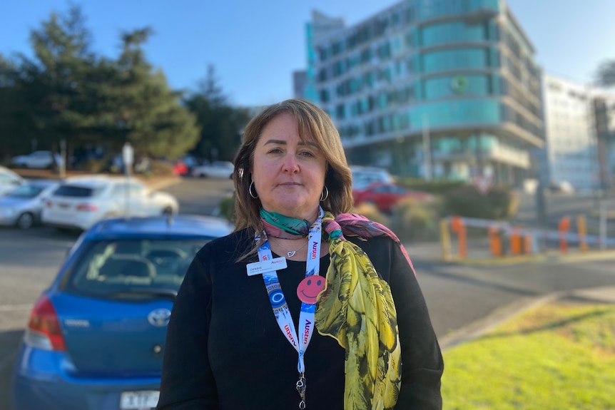 a woman with brown hair wearing a colourful scarf. She is standing in front of the Olivia Newton-John research centre.