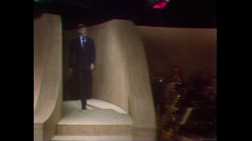 A man in a suit appears at the top of the stairs.