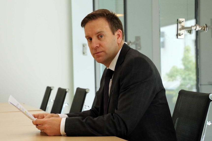 Chris Kent looks at the camera while sitting at a row of desks in a boardroom.